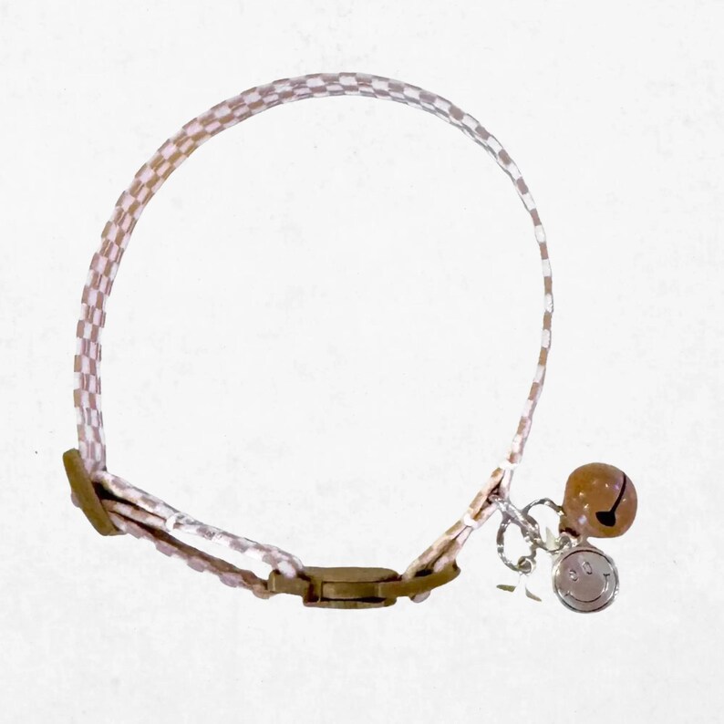 A checkered cat collar with a bell attached, featuring a round bell charm.