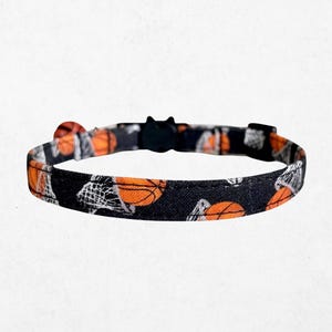 A black and orange patterned cat collar with basketballs printed on it.