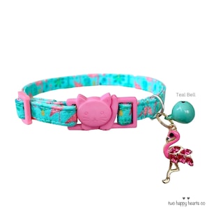 May include: A teal cat collar with a pink cat-shaped buckle and a flamingo charm. The collar has a pattern of pink flamingos and green leaves. A teal bell hangs from the collar.