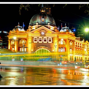 Pu&ograve; includere: Una vista notturna di un grande edificio ornato con una torre dell'orologio. L'edificio &egrave; illuminato da luci gialle calde, e in primo piano ci sono auto e lampioni. L'edificio si riflette sul selciato bagnato.