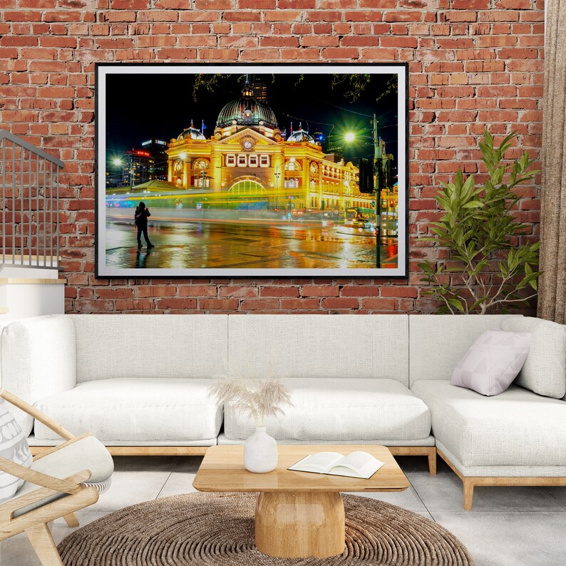 Pu&ograve; includere: Una fotografia incorniciata di un grande edificio illuminato con una torre dell'orologio di notte. L'edificio si riflette in una strada bagnata, e c'&egrave; una persona che cammina in primo piano.