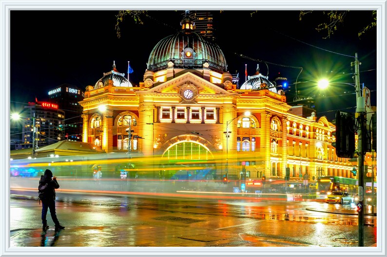 Pu&ograve; includere: Una vista notturna di un grande edificio ornato con una torre dell'orologio e una cupola. L'edificio &egrave; illuminato da luci gialle calde, e in primo piano ci sono auto e lampioni. L'edificio si riflette sul selciato bagnato.