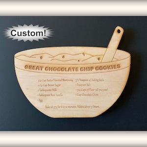 May include: Wooden bowl-shaped cookie cutter with the text "GREAT CHOCOLATE CHIP COOKIES" and a list of ingredients and instructions for baking chocolate chip cookies. The cutter is brown and has a spoon handle.