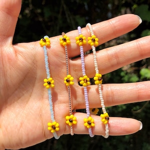 May include: Five beaded bracelets with yellow sunflower charms. The bracelets are in shades of blue, white, pink, and gold.