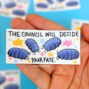 May include: A rectangular sticker featuring three blue pill bugs with segmented bodies. The text reads THE COUNCIL WILL DECIDE YOUR FATE in black capital letters. The design includes small yellow and pink star-shaped accents on a white background.