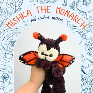 May include: A crochet plush toy shaped like a butterfly with dark brown yarn, a cream-colored face, and orange-tipped antennae. The wings feature orange and black patterns with white spots. The text reads MISHKA THE MONARCH pdf crochet pattern.