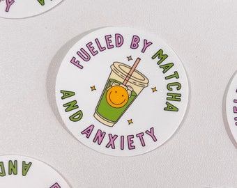 May include: Circular white stickers featuring a matcha drink cartoon with a smiling face. The text "FUELED BY MATCHA AND ANXIETY" is printed around the image. The stickers have a straw and star accents. The stickers are a fun, quirky design.