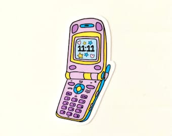 May include: A pink and yellow cartoon flip phone with a screen displaying the time 11:11. The screen also has small hearts and stars. The phone has a keypad with purple buttons.