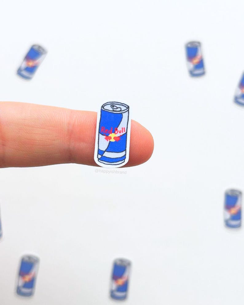 Puede incluir: Una pegatina en miniatura de una lata de bebida energ&eacute;tica Red Bull. La lata es principalmente azul con detalles blancos y rojos, con el logotipo de Red Bull. Varias pegatinas similares m&aacute;s est&aacute;n dispersas en el fondo.