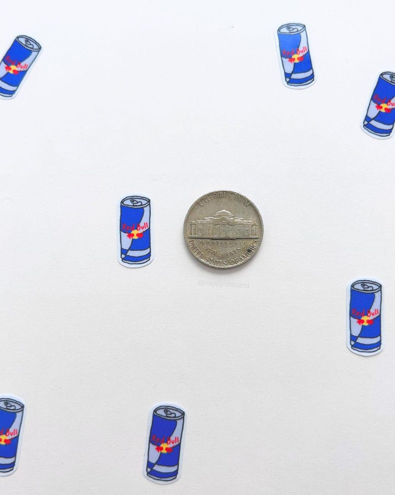 Puede incluir: Una colecci&oacute;n de peque&ntilde;as pegatinas de latas de Red Bull azules y blancas con un logotipo rojo, dispersas alrededor de una moneda de n&iacute;quel sobre un fondo blanco. Las pegatinas est&aacute;n en varias orientaciones.