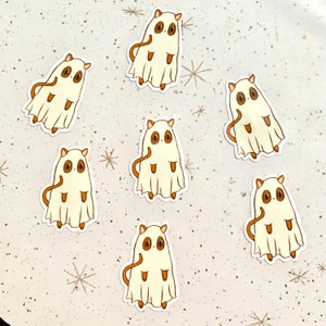 May include: Seven stickers featuring a cartoon ghost-like creature with brown eyes, ears, and tail. The creature is covered in a white sheet with a tan outline. The stickers are arranged on a speckled, off-white surface with star-shaped accents.