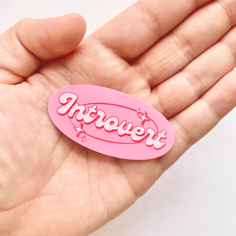 May include: Pink oval sticker with the word "Introvert" in white letters with a pink outline. The sticker has a white star design around the word.
