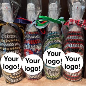 May include: Four glass bottles wrapped in clear plastic, each decorated with rows of colorful rhinestones. The bottles feature ribbons tied around the necks and white circular labels with the text Your logo! printed on the front of each bottle.