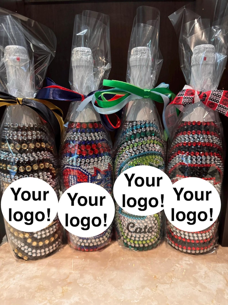 May include: Four glass bottles wrapped in clear plastic, each decorated with rows of colorful rhinestones. The bottles feature ribbons tied around the necks and white circular labels with the text Your logo! printed on the front of each bottle.