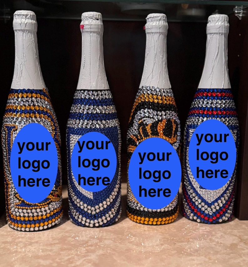 May include: Four glass bottles with white foil-wrapped necks, each fully covered in small, colorful rhinestones arranged in distinct patterns. Each bottle features a prominent blue oval overlay in the center with the text your logo here.