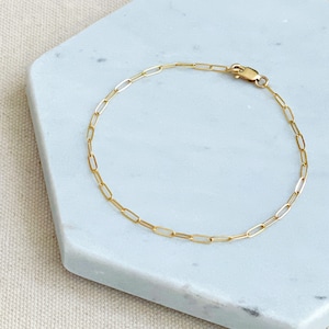 May include: A gold chain bracelet with a lobster clasp closure. The bracelet is made of small, linked oval shapes.