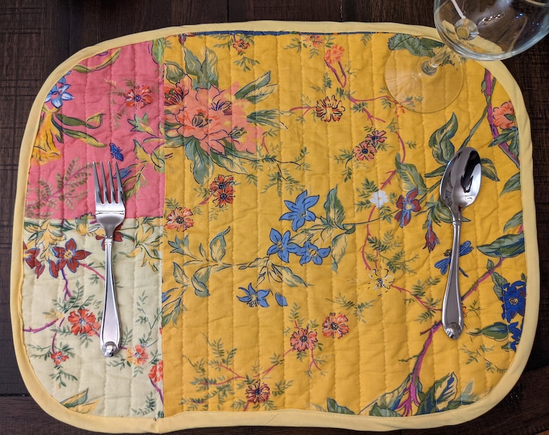 Add a touch of vibrancy to your dining table with this handmade in the USA reversible placemat set. The set features a cheerful patchwork design with floral patterns in red, yellow, blue, and pink, ideal for festive occasions and everyday use.