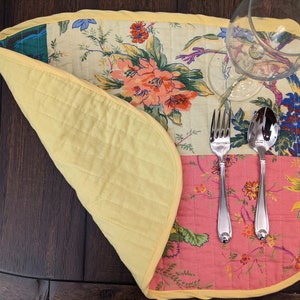Elegant handcrafted placemat with a colorful patchwork of floral prints in red, pink, yellow, and green. Finished with a yellow trim, this unique piece adds a touch of charm to your dining table. Ideal for special occasions or everyday use reversible