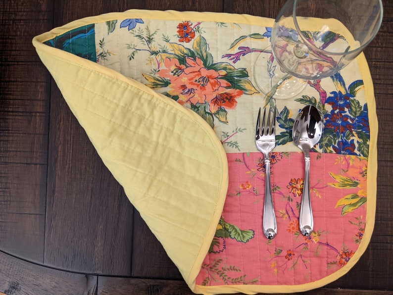 Elegant handcrafted placemat with a colorful patchwork of floral prints in red, pink, yellow, and green. Finished with a yellow trim, this unique piece adds a touch of charm to your dining table. Ideal for special occasions or everyday use reversible