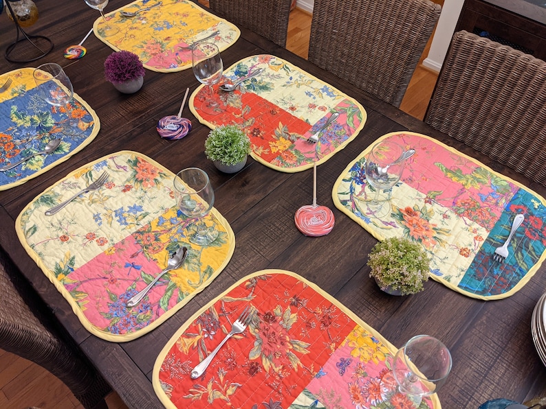 Enhance your dining experience with this reversible placemat set, handcrafted in the USA. The set features a striking patchwork design with bold floral patterns in red, yellow, blue, and pink, adding a burst of color to any table setting. Tropical floral print placemat close‑up in quilted cotton patchwork, ideal for summer dinner parties, picnics, and everyday use