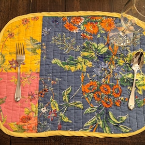 Handcrafted in the USA, this reversible placemat set features a colorful patchwork design with floral patterns in bright shades of red, yellow, blue, and pink. Perfect for creating a lively and inviting dining atmosphere.