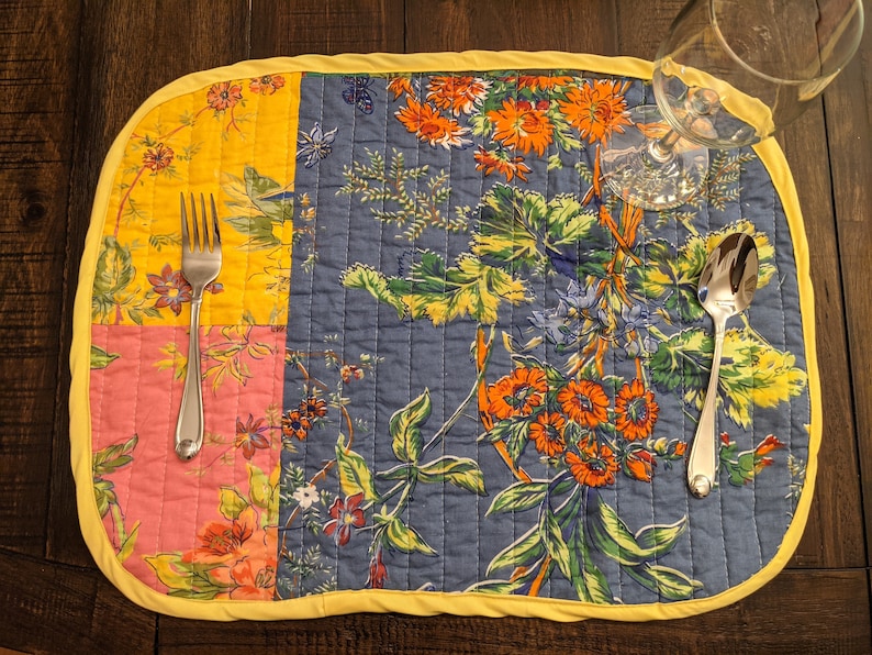 Handcrafted in the USA, this reversible placemat set features a colorful patchwork design with floral patterns in bright shades of red, yellow, blue, and pink. Perfect for creating a lively and inviting dining atmosphere.