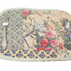May include: A green quilted placemat with a floral pattern featuring pink, red, yellow, and blue flowers. A silver fork and spoon are placed on the placemat.