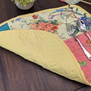 Vibrant handcrafted placemat featuring a patchwork of floral designs in red, pink, yellow, and green, bordered with a cheerful yellow trim. This elegant piece is ideal for brightening up any dining experience. Proudly made in the USA. Eclectic patchwork placemats set combining vintage floral prints and solid color blocks, finished with sunny yellow binding for lively table décor