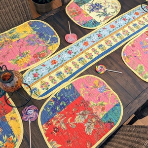 K&ouml;nnte beinhalten: Ein Set aus bunten, gesteppten Platzsets mit Blumenmuster und einem passenden Tischl&auml;ufer. Die Platzsets sind oval geformt und der L&auml;ufer ist rechteckig. Das Blumenmuster ist eine Mischung aus Rosa, Gelb, Blau und Gr&uuml;n.