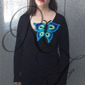 May include: A black sweater with a crocheted butterfly brooch. The butterfly is blue, green, and yellow.