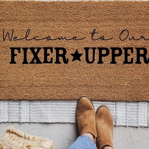 May include: A brown doormat with the text "Welcome to Our Fixer Upper" in black lettering with a star between the words "Fixer" and "Upper".