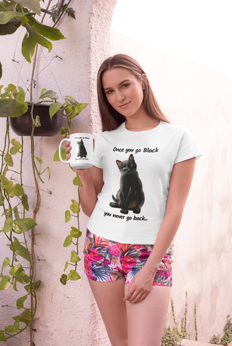 May include: White t-shirt with a black cat graphic and the text "Once you go Black you never go back...". The image also shows a white mug with the same cat graphic. The person is wearing floral shorts.