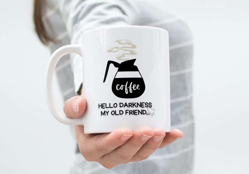May include: White ceramic coffee mug with a black and white illustration of a coffee pot with steam coming out of it. The text "coffee" is written on the pot. The text "Hello darkness my old friend" is written below the pot.