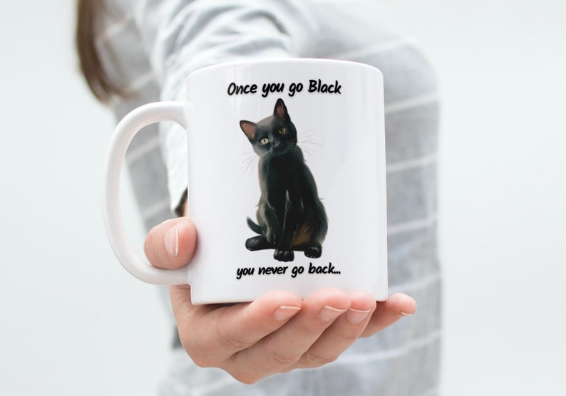 May include: White ceramic mug featuring a black cat illustration with the text "Once you go Black you never go back...". The cat has yellow eyes and is sitting upright. The mug has a white handle.