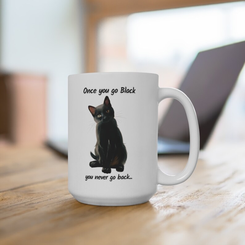 May include: White ceramic mug featuring a black cat illustration with the text "Once you go Black you never go back...". The mug has a large handle and is sitting on a wooden surface.