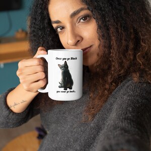 May include: White ceramic mug featuring a black cat illustration with the text "Once you go Black you never go back...". The mug has a large handle and is held by a person. The mug is a standard size for coffee or tea.