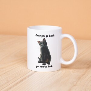May include: White ceramic mug featuring a black cat illustration with the text "Once you go Black you never go back." The cat is depicted with yellow eyes and a sleek black coat. The mug has a curved handle.