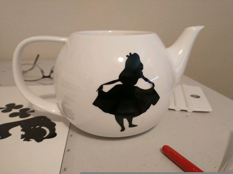 Pu&ograve; includere: Teiera in ceramica bianca con una silhouette nera di una ragazza con un vestito. La teiera ha un corpo arrotondato, un manico curvo e un beccuccio. Il design &egrave; probabilmente ispirato a un personaggio di fiaba.