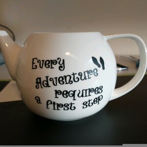 Pu&ograve; includere: Teiera in ceramica bianca con corpo arrotondato, beccuccio e manico. La teiera presenta un testo nero che recita "Every Adventure requires a first step" con impronte nere. Un affascinante accessorio da cucina.