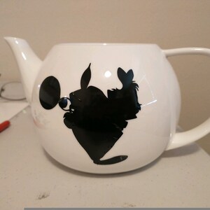 Pu&ograve; includere: Teiera in ceramica bianca con una silhouette nera di un personaggio dei cartoni animati. La teiera ha un corpo arrotondato, un manico curvo e un beccuccio. La silhouette &egrave; sul davanti.
