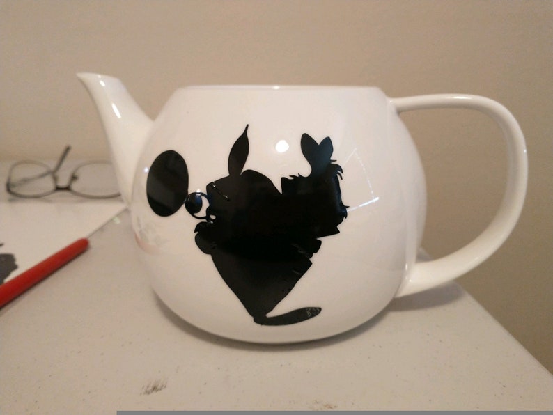 Pu&ograve; includere: Teiera in ceramica bianca con una silhouette nera di un personaggio dei cartoni animati. La teiera ha un corpo arrotondato, un manico curvo e un beccuccio. La silhouette &egrave; sul davanti.