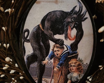 May include: A vintage illustration of a black devil with a long red tongue, holding a child in a blue sailor shirt and a basket. A young girl in a blue dress stands nearby. The illustration is framed in a black oval and surrounded by a wreath of white berries.