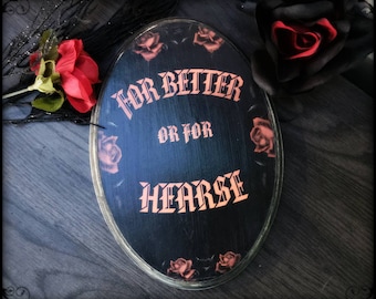 Puede incluir: Un letrero de madera ovalado negro con el texto "For Better Or For Hearse" en letras naranjas. El letrero está decorado con rosas rojas.