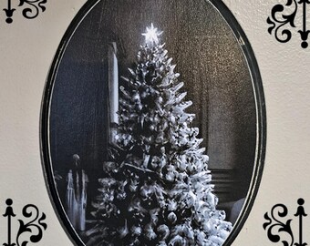 Puede incluir: Una fotografía en blanco y negro de un árbol de Navidad decorado con adornos y regalos debajo. El árbol está en un marco ovalado con un borde decorativo.