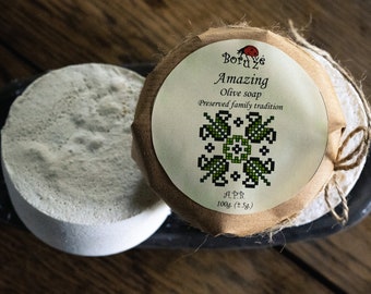 May include: A round bar of olive soap wrapped in brown paper with a label that reads "Bord ve Amazing Olive soap Preserved family tradition APB. 100g. (±5g.)".
