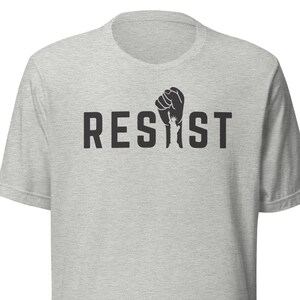 May include: A heather grey t-shirt with a black fist graphic and the word "RESIST" printed on the front.