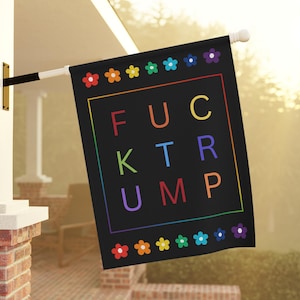 May include: Black flag with the text "FUCK TRUMP" in rainbow colors, framed by a rainbow border and flower accents. The flag is hanging outside on a white pole.