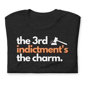 May include: Black t-shirt with white text that reads "the 3rd indictment's the charm."  A white gavel with an orange handle is above the text.
