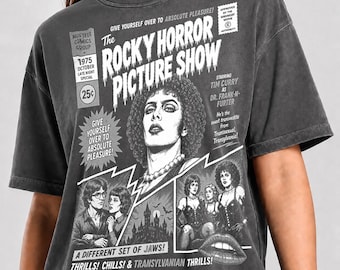 May include: A charcoal grey t-shirt featuring a graphic print inspired by The Rocky Horror Picture Show. The design includes the movie title, a portrait of Dr. Frank-N-Furter, comic-style panels, and text including "Give yourself over to absolute pleasure."
