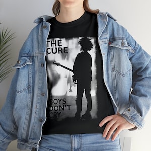 Puede incluir: Camiseta negra con un gráfico blanco de una silueta de una persona tocando una guitarra. El texto "The Cure" y "Boys Don't Cry" está impreso en la camiseta.